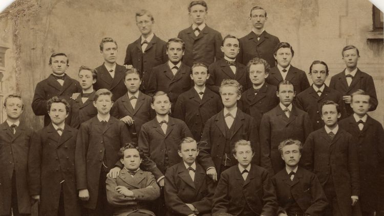 Das Bild zeigt die ausschließlich männlichen Absolventen des Jahrganges 1884 des alten Lehrerseminars. Sie sitzen beziehungsweise stehen und schauen in die Kamera. Alle tragen Anzug und Krawatte. Vor Ihnen steht ein Fass mit der Aufschrift "1880 bis 1884".